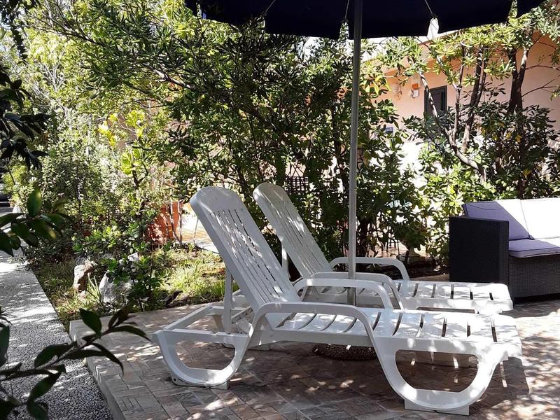 Due sdraio bianche sotto un ombrellone blu su una terrazza con alberi.