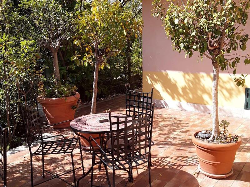 Terrazza con tavolo e sedie in ferro, circondata da piante in vaso sotto gli alberi.