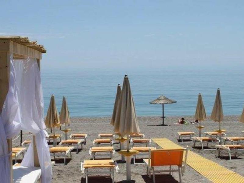 Lettini vuoti e ombrelloni chiusi sulla spiaggia con vista sul mare.