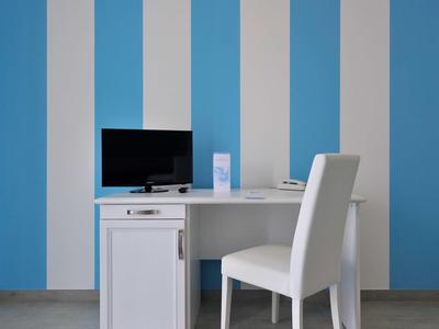 Weißer Schreibtisch mit schwarzem Monitor und weißem Stuhl vor blau-weiß gestreifter Wand.