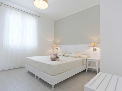 Ein helles Schlafzimmer mit weißem Bett, Nachttischlampen und einem Fenster mit Vorhang.