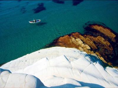 Klares blaues Wasser mit Boot und felsiger, weißer Küstenformation im Vordergrund.