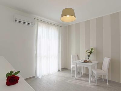 Heller Raum mit gestreifter Wand, kleinem Tisch, zwei Stühlen, Blumenvase und Luftklimaanlage.