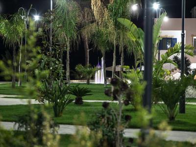 Nächtlicher Park mit Palmen, Grasflächen und beleuchteten Wegen unter Laternen.