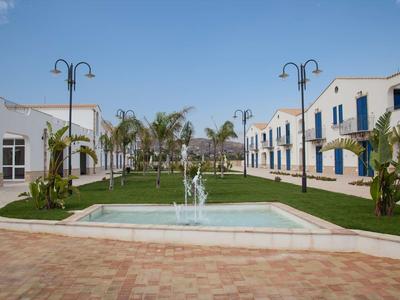 Innenhof mit Springbrunnen, grünen Rasenflächen, Palmen und weißen Gebäuden unter blauem Himmel.