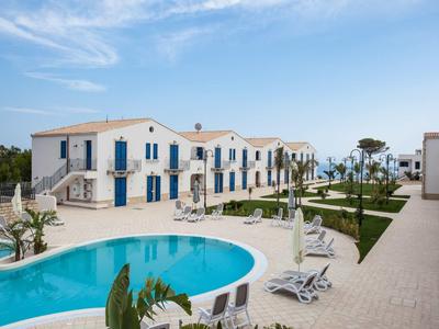 Moderní hotelový komplex s pohodlnými pokoji, bazénem a lehátky pod modrou oblohou.