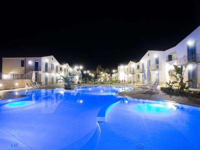 Pool mit blauem Licht umgeben von weißen Häusern und Laternen in einer ruhigen Nacht.