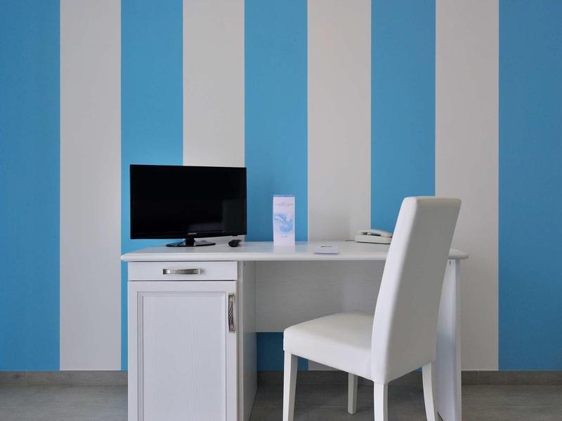 Weißer Schreibtisch mit schwarzem Monitor und weißem Stuhl vor blau-weiß gestreifter Wand.