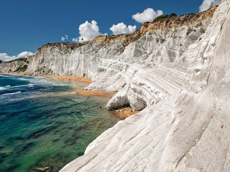 Weiße Felsenklippen treffen auf türkisblaues Meer unter blauem Himmel mit Wolken.