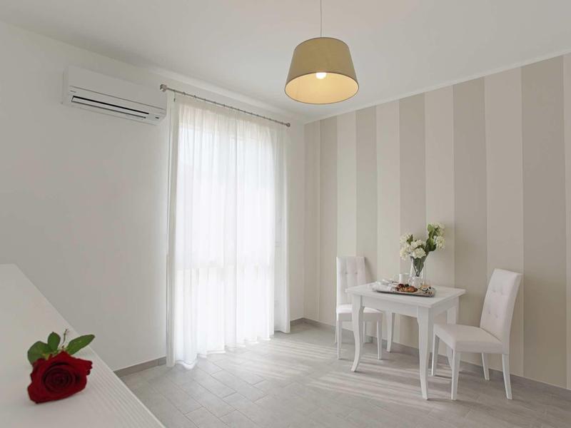 Heller Raum mit gestreifter Wand, kleinem Tisch, zwei Stühlen, Blumenvase und Luftklimaanlage.