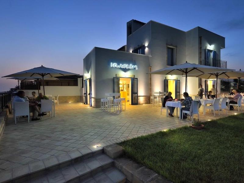 Modernes Restaurant mit Terrasse, beleuchtet bei Dämmerung, Gäste sitzen unter Schirmen.