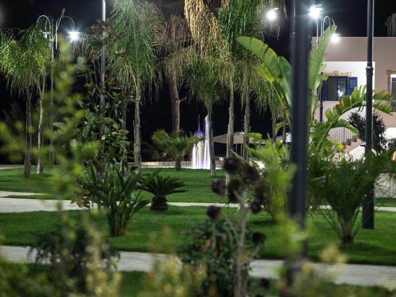 Nächtlicher Park mit Palmen, Grasflächen und beleuchteten Wegen unter Laternen.