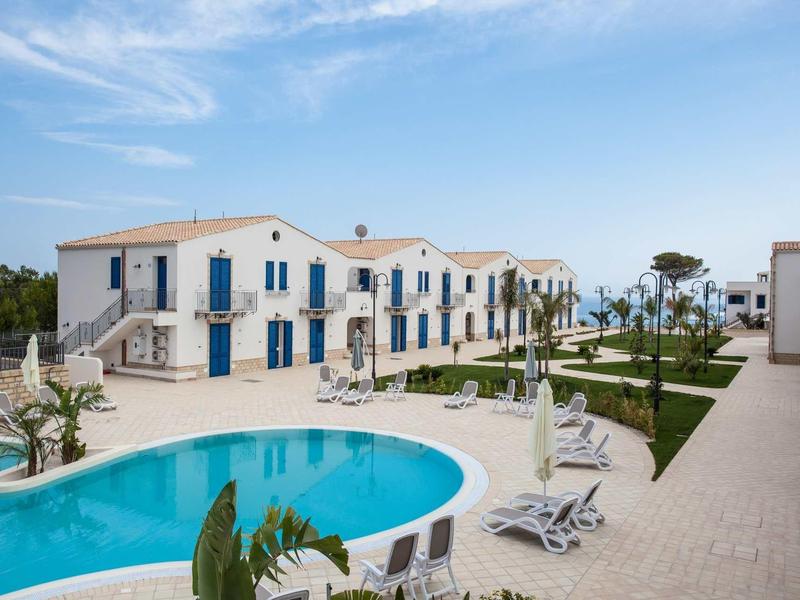 Moderner Ferienkomplex mit rundem Pool, weißen Gebäuden und blauem Himmel im Hintergrund.