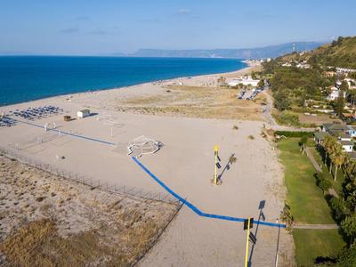 Ampia spiaggia di sabbia con rete da pallavolo e area verde adiacente vicino al mare.