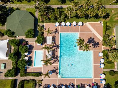 Veduta aerea di una piscina d'hotel con lettini, ombrelloni e paesaggio verde circostante.