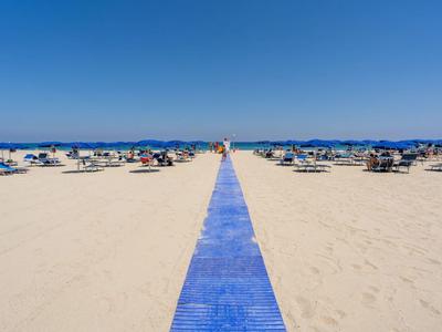 Un lungo e largo sentiero blu attraversa una spiaggia di sabbia chiara con ombrelloni e sdraio.