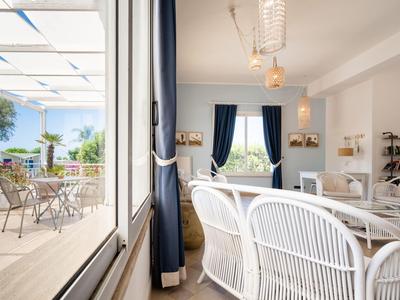 Sala da pranzo luminosa con sedie di vimini bianche, tende blu e terrazza esterna con mobili da giardino.