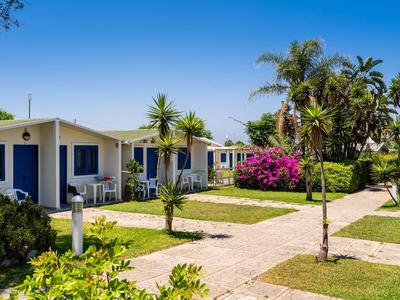 Diversi bungalow per vacanze con porte blu in un giardino tropicale sotto un cielo limpido.