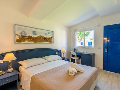 Camera d'hotel luminosa con letto matrimoniale, porta blu e finestra con vista.