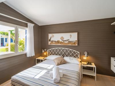 Camera d'hotel luminosa con letto matrimoniale, parete in legno, comodini e finestra aperta con vista sul verde.