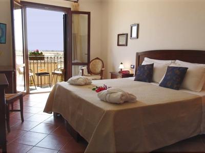 Jasny pokój hotelowy z podwójnym łóżkiem, dwoma szlafrokami i balkonem z widokiem na morze.