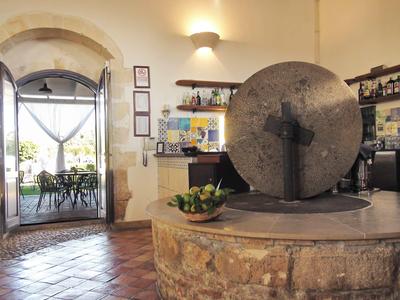 Rustykalne lobby hotelowe z kamieniem młyńskim i widokiem na taras z krzesłami.