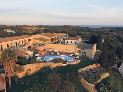 Kompleks hotelowy z basenem i otaczającą przyrodą na pagórkowatym terenie o zachodzie słońca.