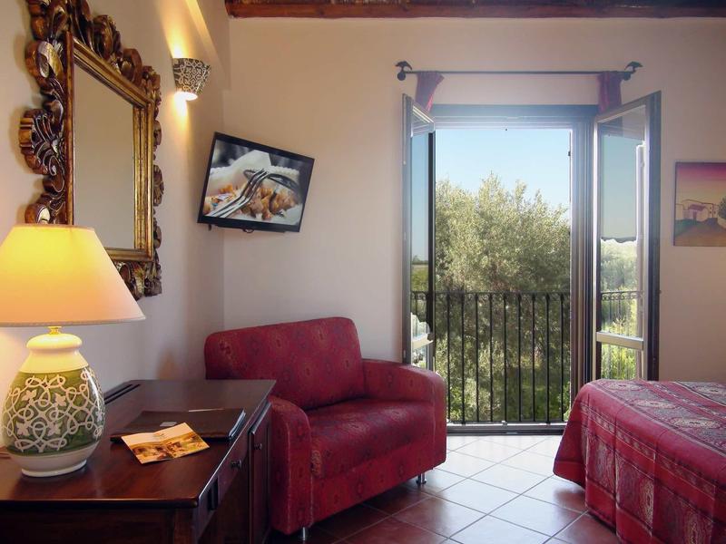 Przytulny pokój hotelowy z czerwonym sofą, dużym lustrem, balkonem i lampką na stoliku.