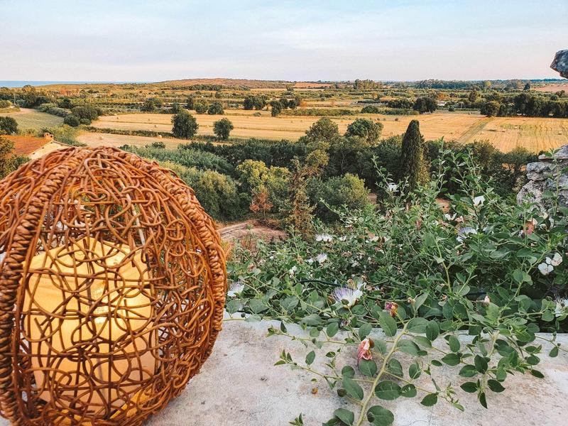 Oświetlony, kulisty kosz z rattanu na tarasie z widokiem na pola i drzewa o zachodzie słońca.