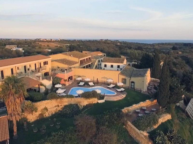 Kompleks hotelowy z basenem i otaczającą przyrodą na pagórkowatym terenie o zachodzie słońca.