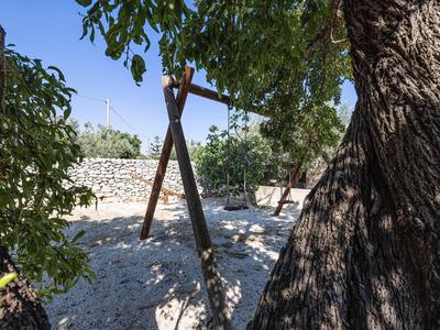 Schaukel befestigt an hölzernen Stangen unter Bäumen in einem sonnigen Garten mit Kiesboden.
