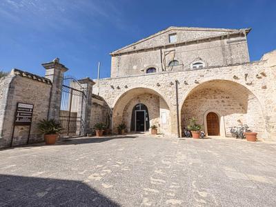 Historisches Gebäude mit großen Bögen und gepflastertem Vorplatz unter blauem Himmel.