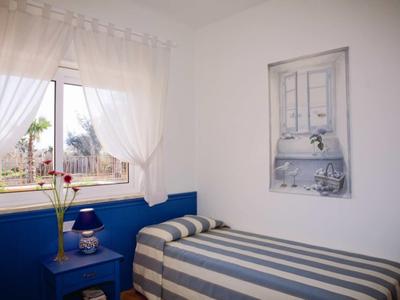 Gezellige eenpersoonskamer met blauw bed, gestreept beddengoed en een raam met witte gordijnen.