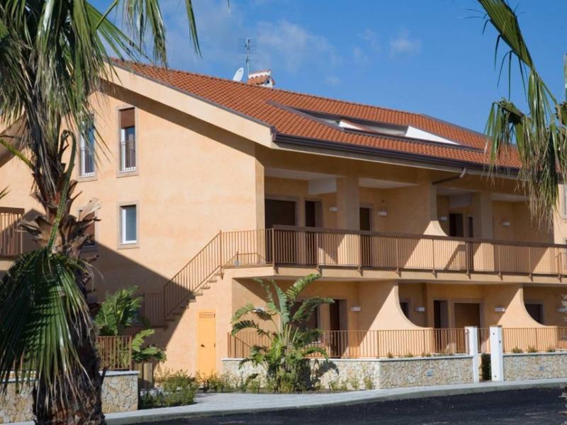 Meerdere verdiepingen tellend hotelgebouw met balkons en palmbomen op een zonnige dag.