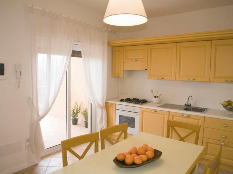 Lichte keuken met gele kasten, eettafel en toegang tot balkon met gordijnen.