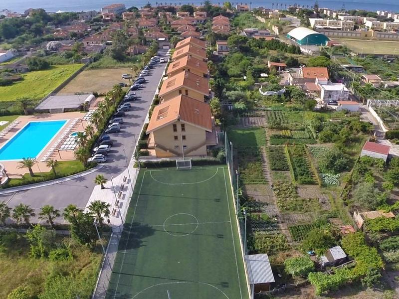 Luchtfoto van een vakantiecomplex met appartementen, zwembad en sportveld naast groen land