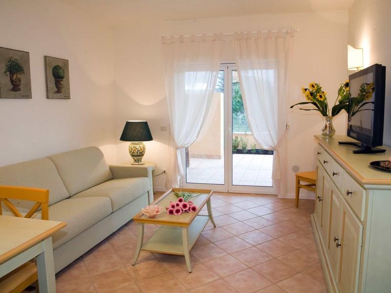 Lichte woonkamer met bank, glazen salontafel, tv en gordijnen bij de terrasdeur.