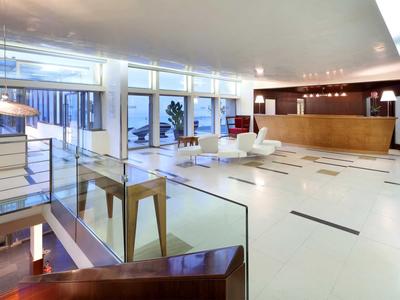 Moderne, helle Empfangshalle mit glatten Fliesen, Holztheke und großen Fensterfronten.