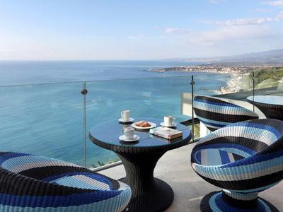 Balkon s kulatými židlemi a stolem na snídani s výhledem na moře a pobřeží.