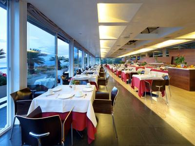 Moderní restaurace s dlouhými okny a prostřenými stoly s výhledem na moře.