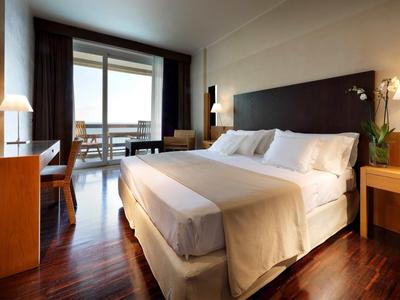 Moderní hotelový pokoj s manželskou postelí, dřevěnou podlahou a balkonem s výhledem na moře.