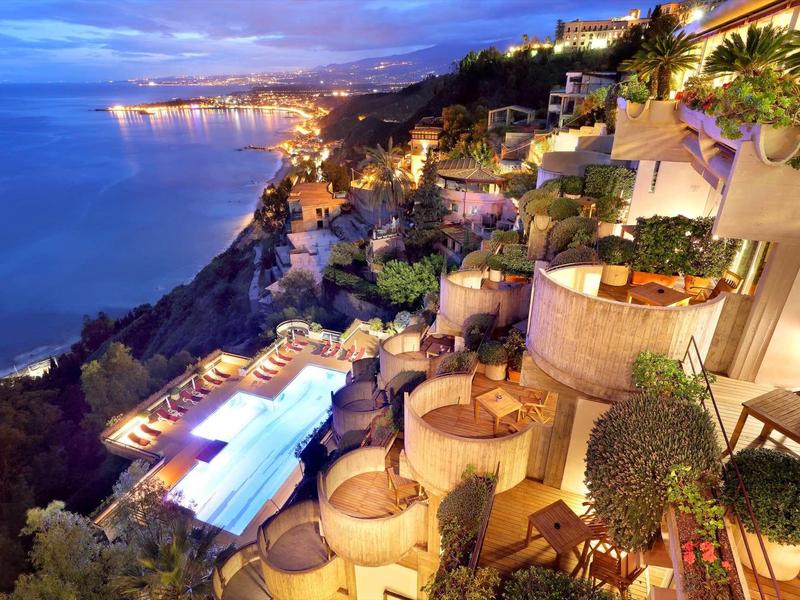 Luxusní hotelová terasa s bazénem s výhledem na osvětlené pobřeží za soumraku