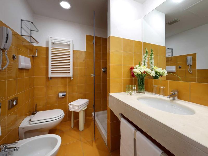 Moderní koupelna s bidetem, toaletou, umyvadlem a béžovou dlažbou.