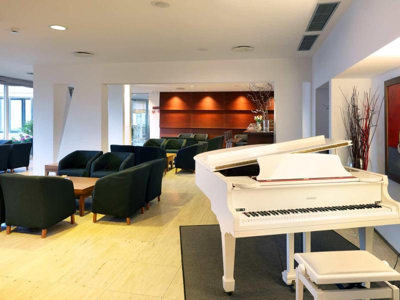 Moderní hotelový lounge s bílým křídlem, sedacími soupravami a velkým oknem.