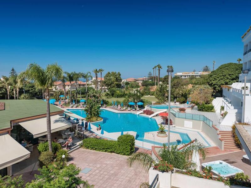 Hotelová bazénová oblast s lehátky a slunečníky pod modrou oblohou.