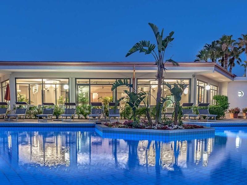 Luxusní hotel s osvětleným bazénem a palmami za soumraku.