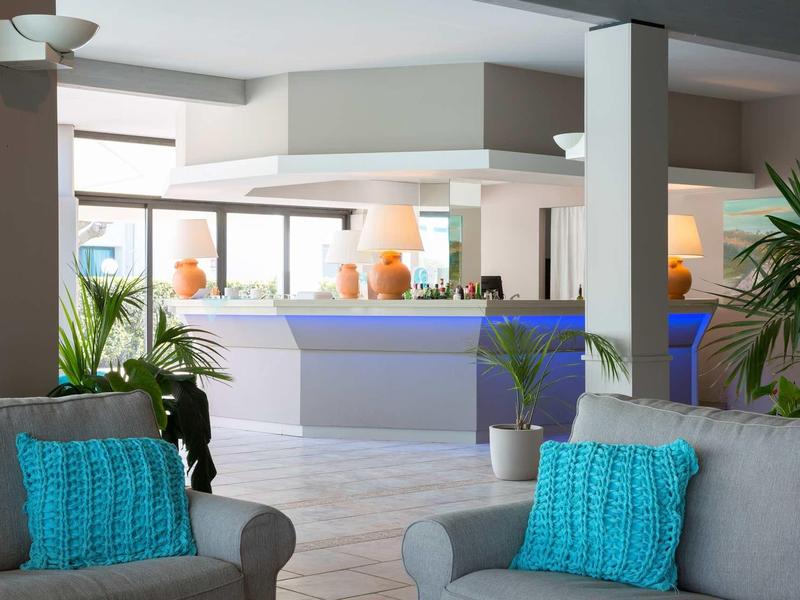 Moderní hotelová lobby se světle šedými křesly a tyrkysovými polštáři u recepce.