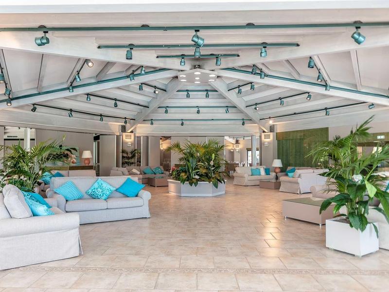 Světlá hala s pohodlnými pohovkami, modrými polštáři a množstvím zelených rostlin.