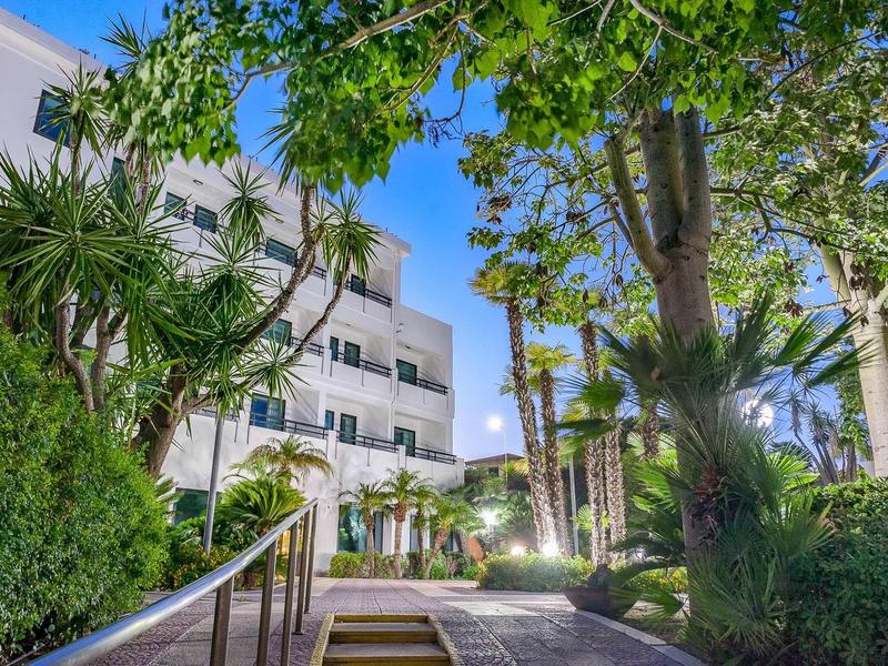 Osvětlená hotelová cesta s palmami a tropickými rostlinami za soumraku.