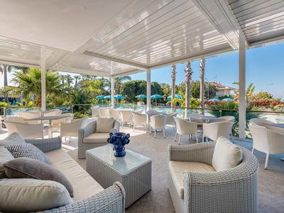 Zadaszony taras z białymi meblami z widokiem na ogród i morze.